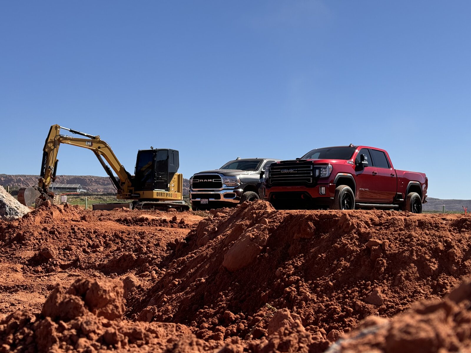 CAT excavator parked alongside the crew's pickups on a red-dirt Southern Utah job site