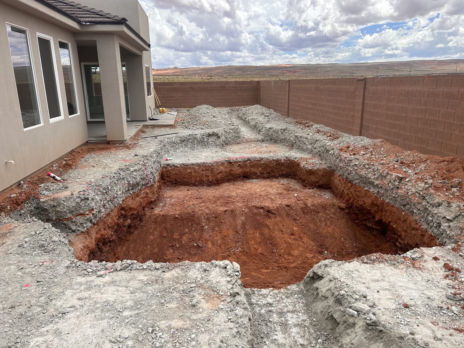 Custom pool shell excavated by Roxor South in a Southern Utah backyard — shallow tanning shelf and deep end carved into the red Apple Valley dirt with block perimeter wall and open mesa beyond