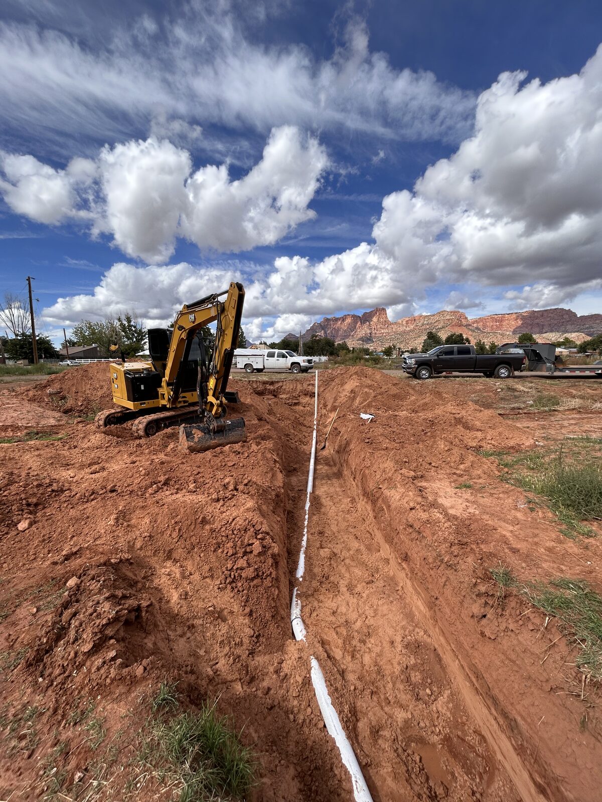 Roxor South mini excavator trenching a long utility run with PVC pipe under Southern Utah red rock cliffs